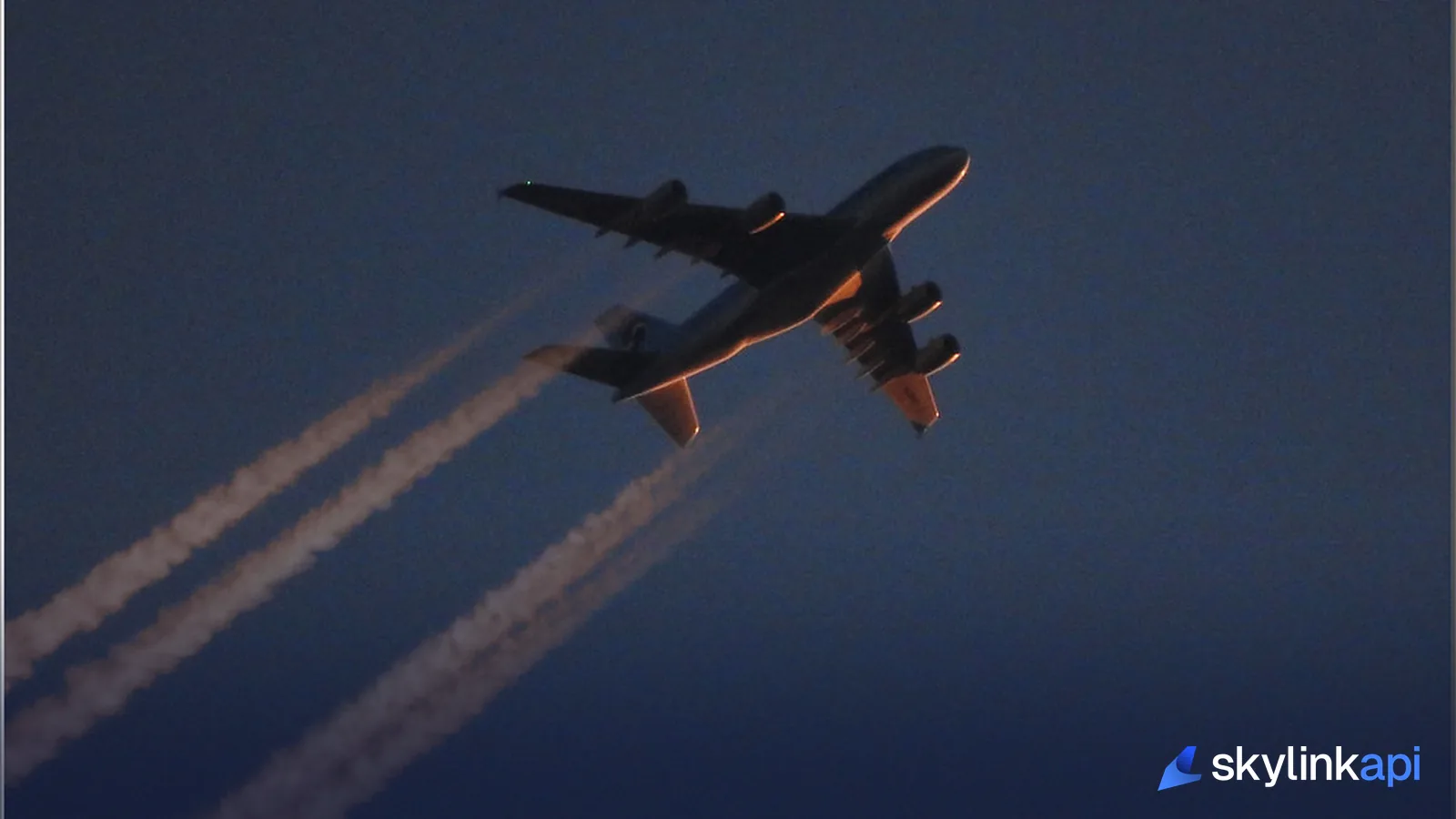 An airliner in flight at dusk, its contrails lit by the setting sun