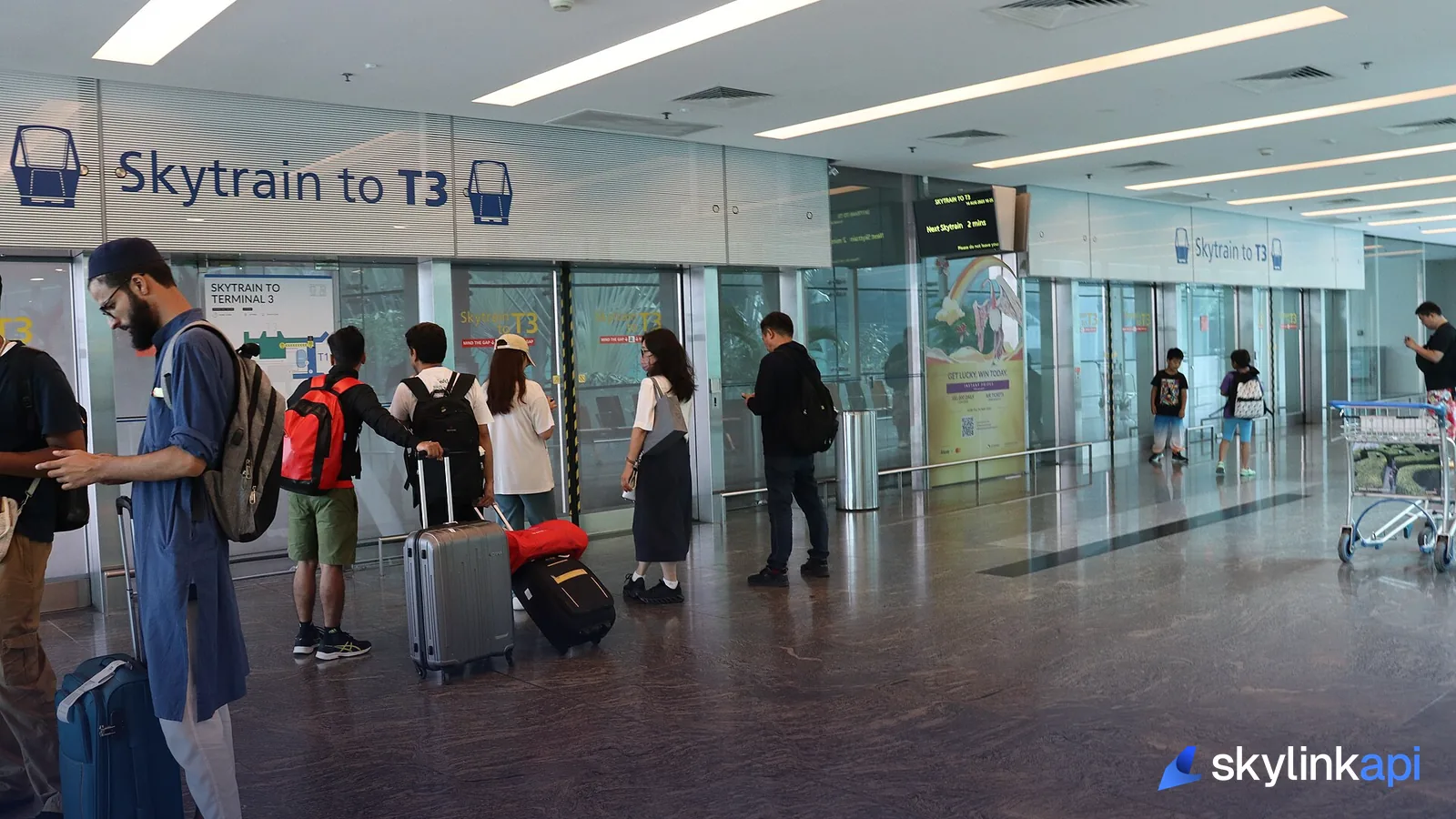 Passengers waiting with luggage in an airport terminal near the skytrain to the gates