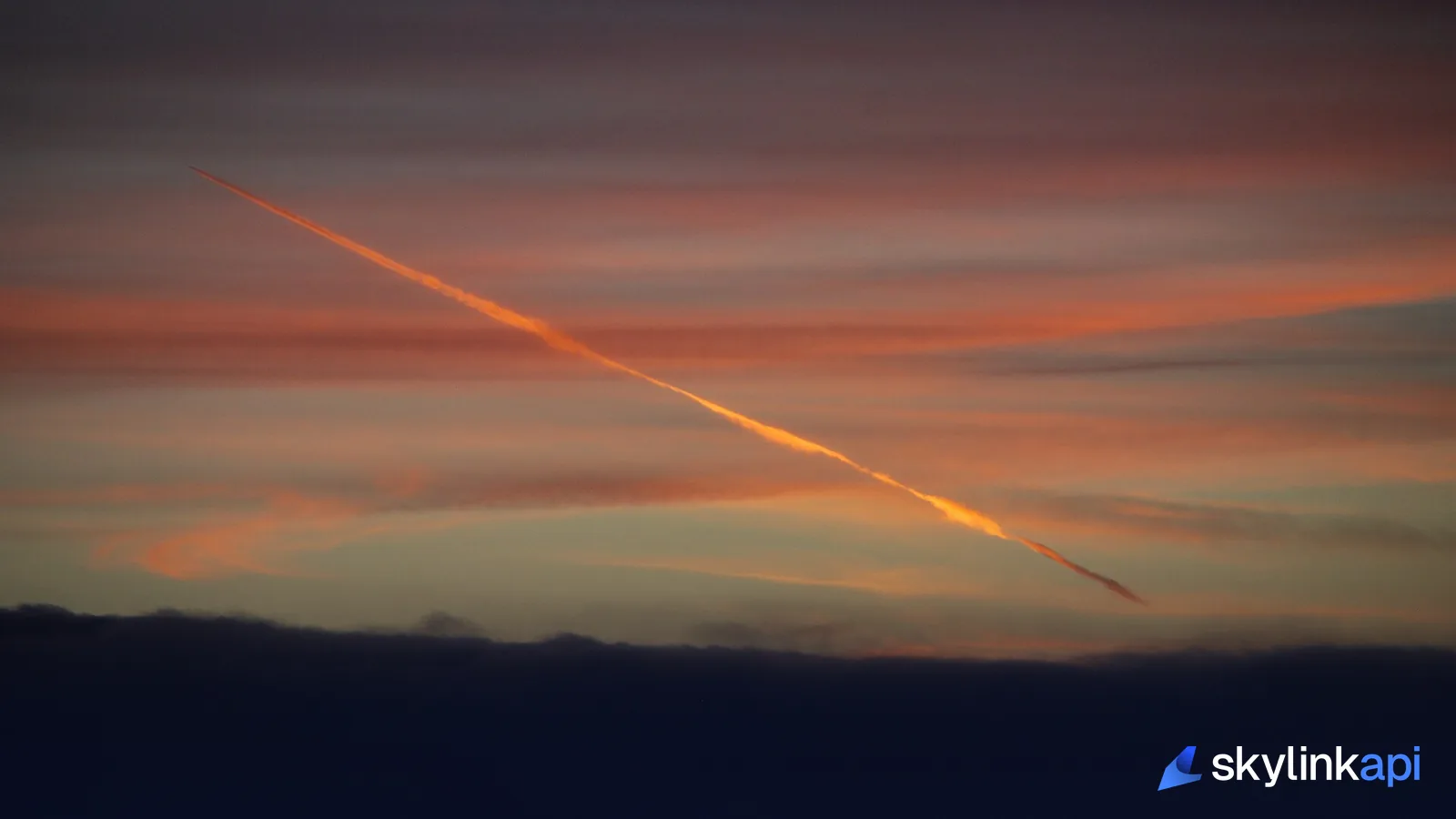A jet contrail lit orange at sunset