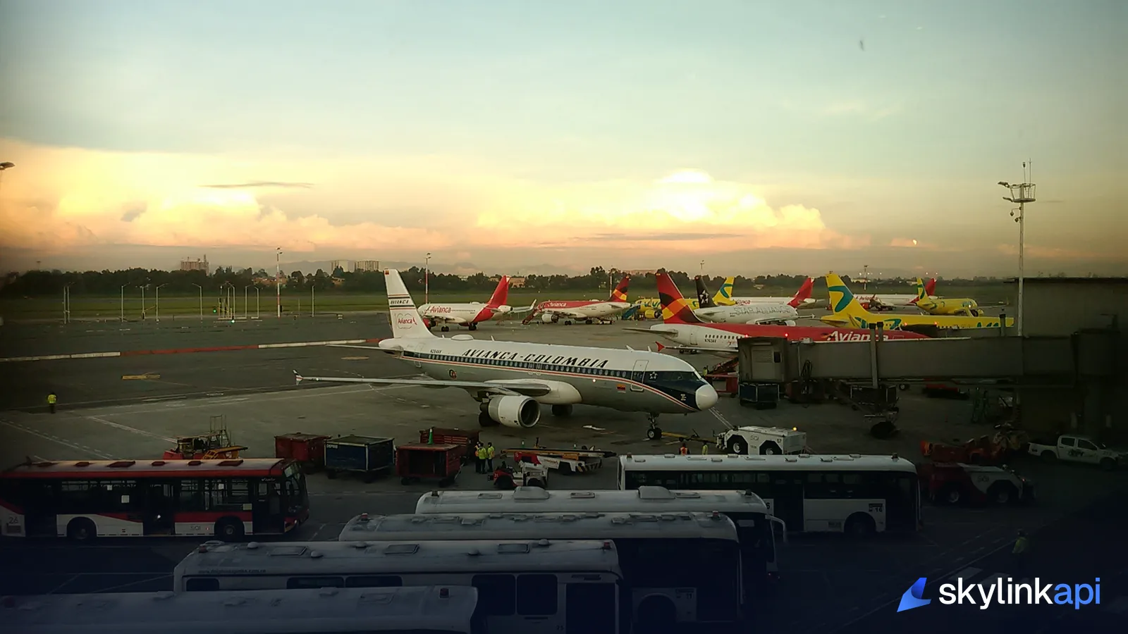 A busy airport apron at dusk with parked aircraft, ground vehicles, and ramp crew