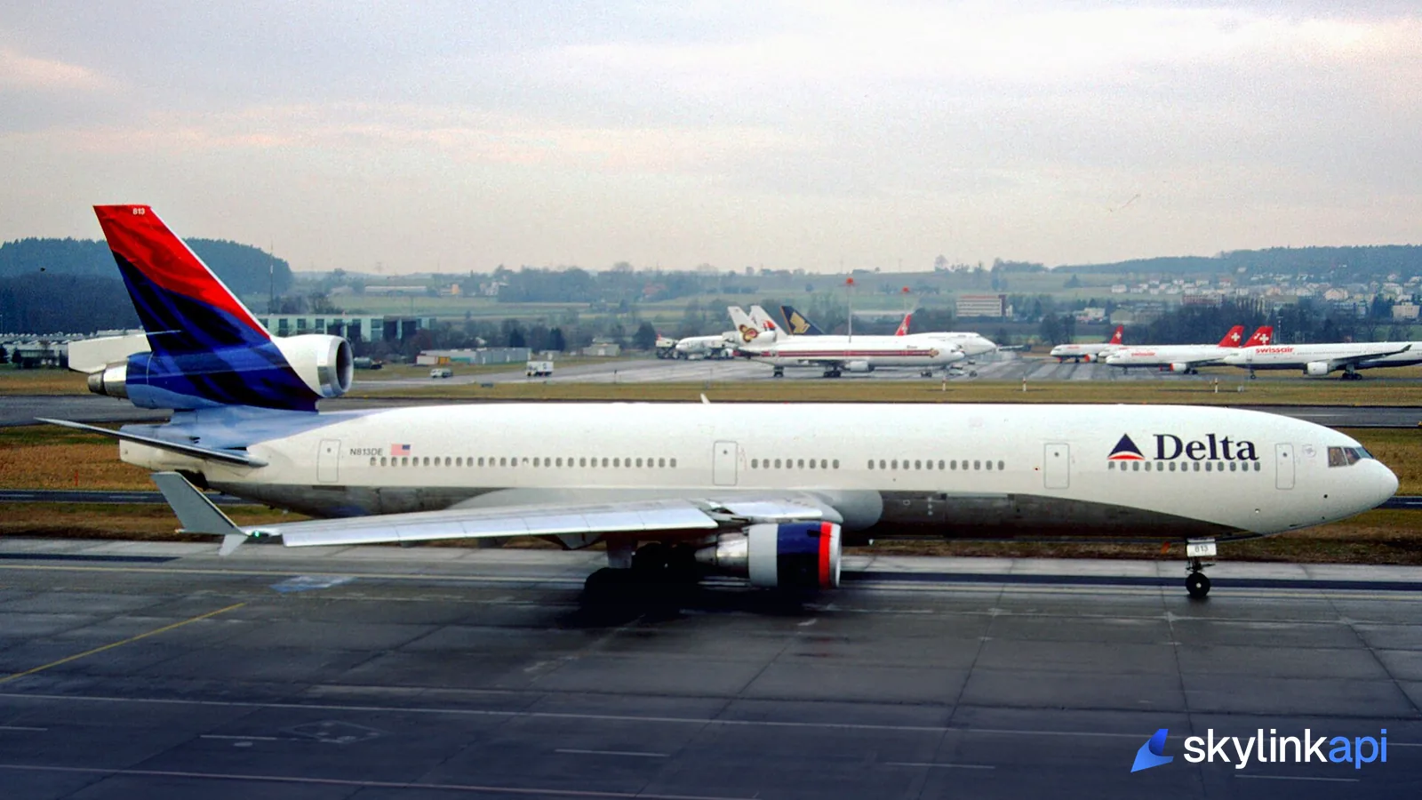 A Delta MD-11 taxiing past a ramp full of parked airliners at a busy airport