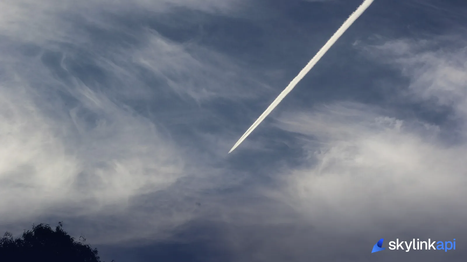 A high-altitude aircraft drawing a long contrail across a wispy sky