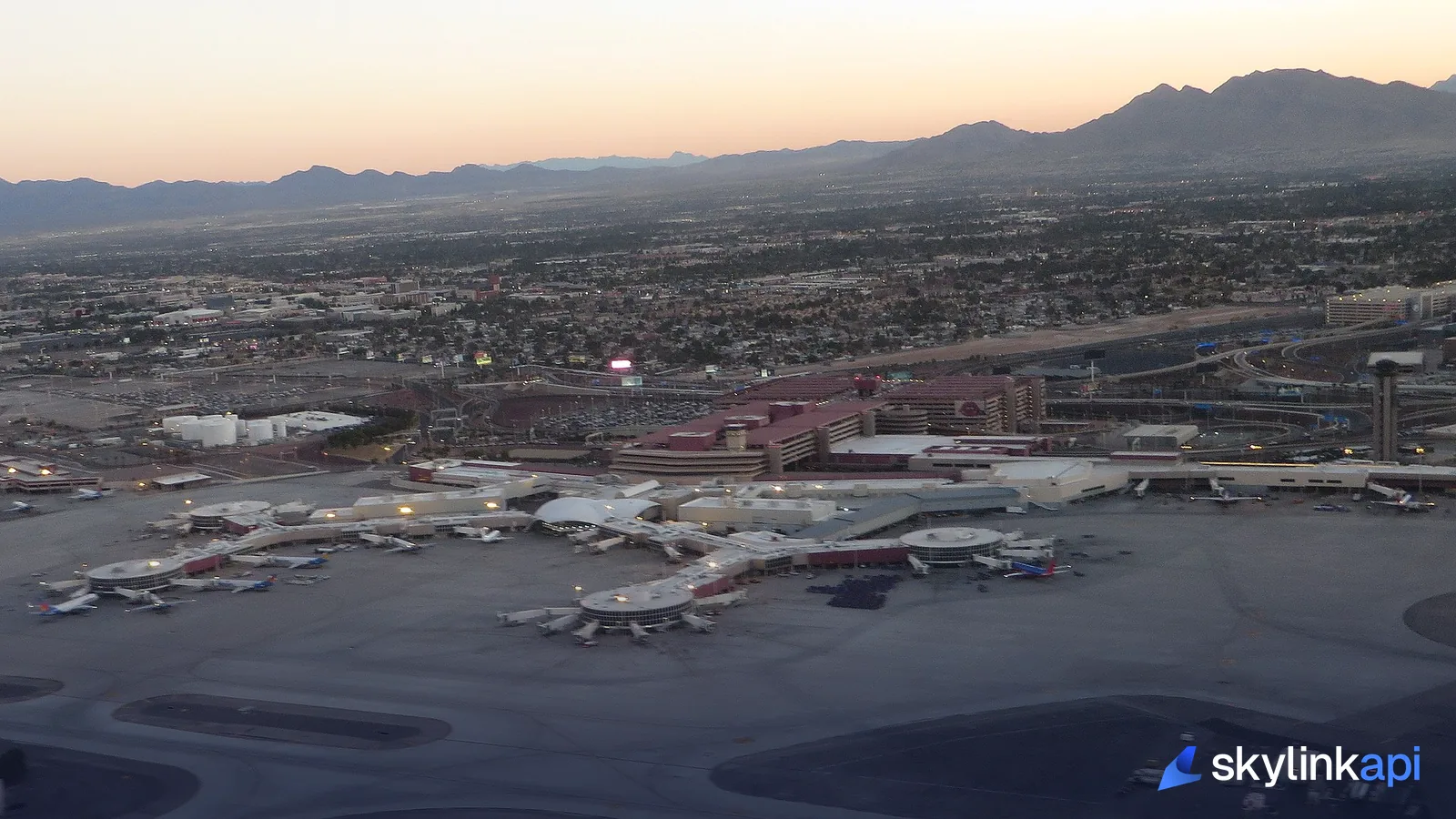 An aerial view of a busy airport terminal ringed with aircraft at its gates, seen from a departing plane
